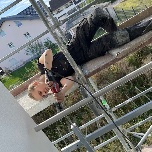 Bella Meier liegt auf einem Gerüst und schweißt ein Geländer zusammen.