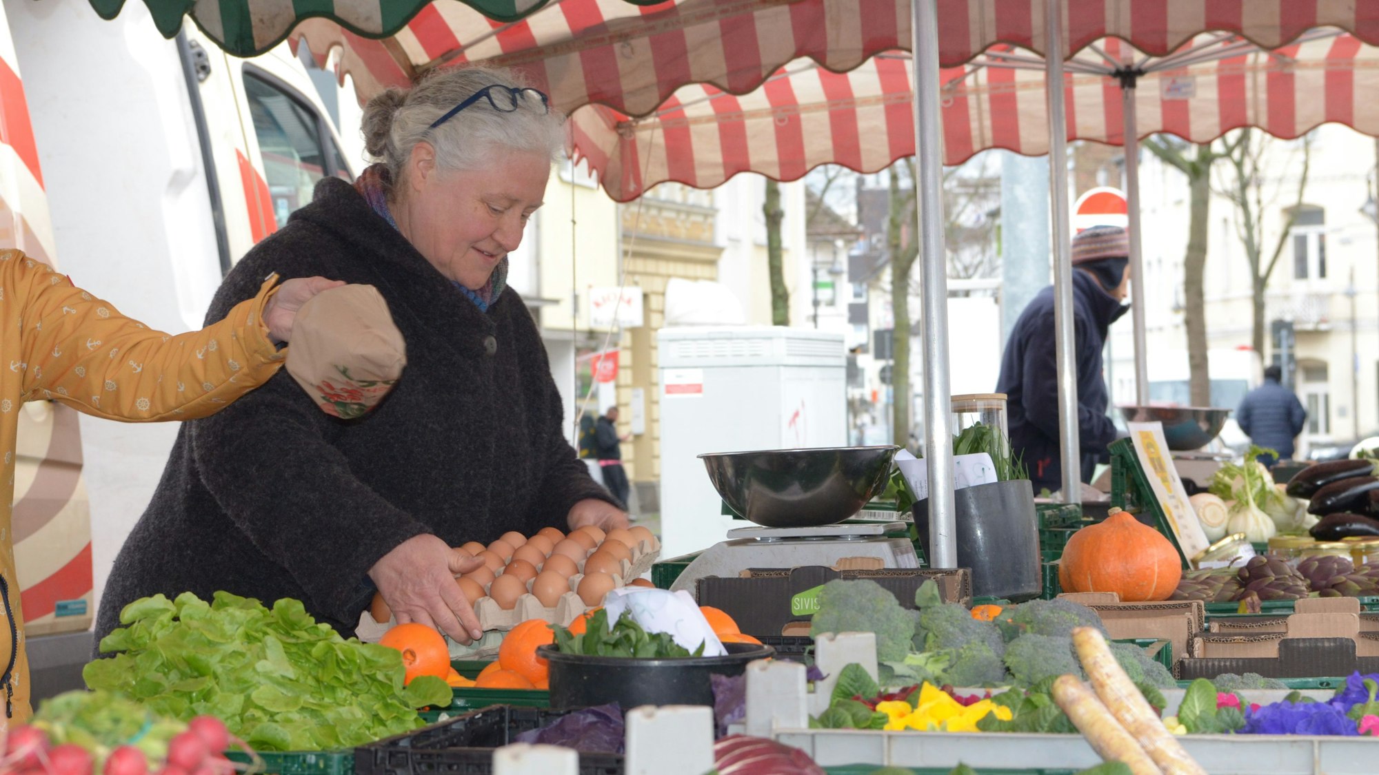 Beate Peters steht hinter ihrem Verkaufsstand mit Obst und Gemüse, sie hält eine Lage Eier in den Händen.