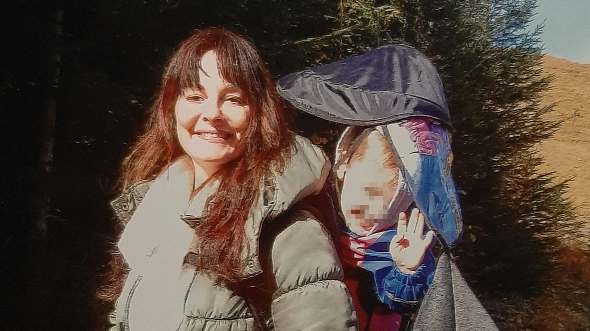 Eine junge Frau steht im Wald, auf ihrem Rücken befördert sie ihren Sohn,