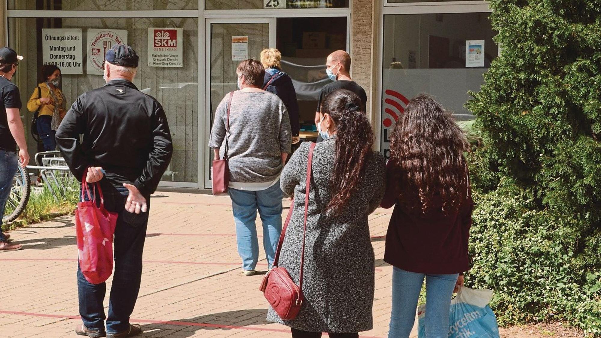 Vor einer Ausgabestelle für Lebensmittel warten Menschen. Sie wenden dem Fotografen den Rücken zu.