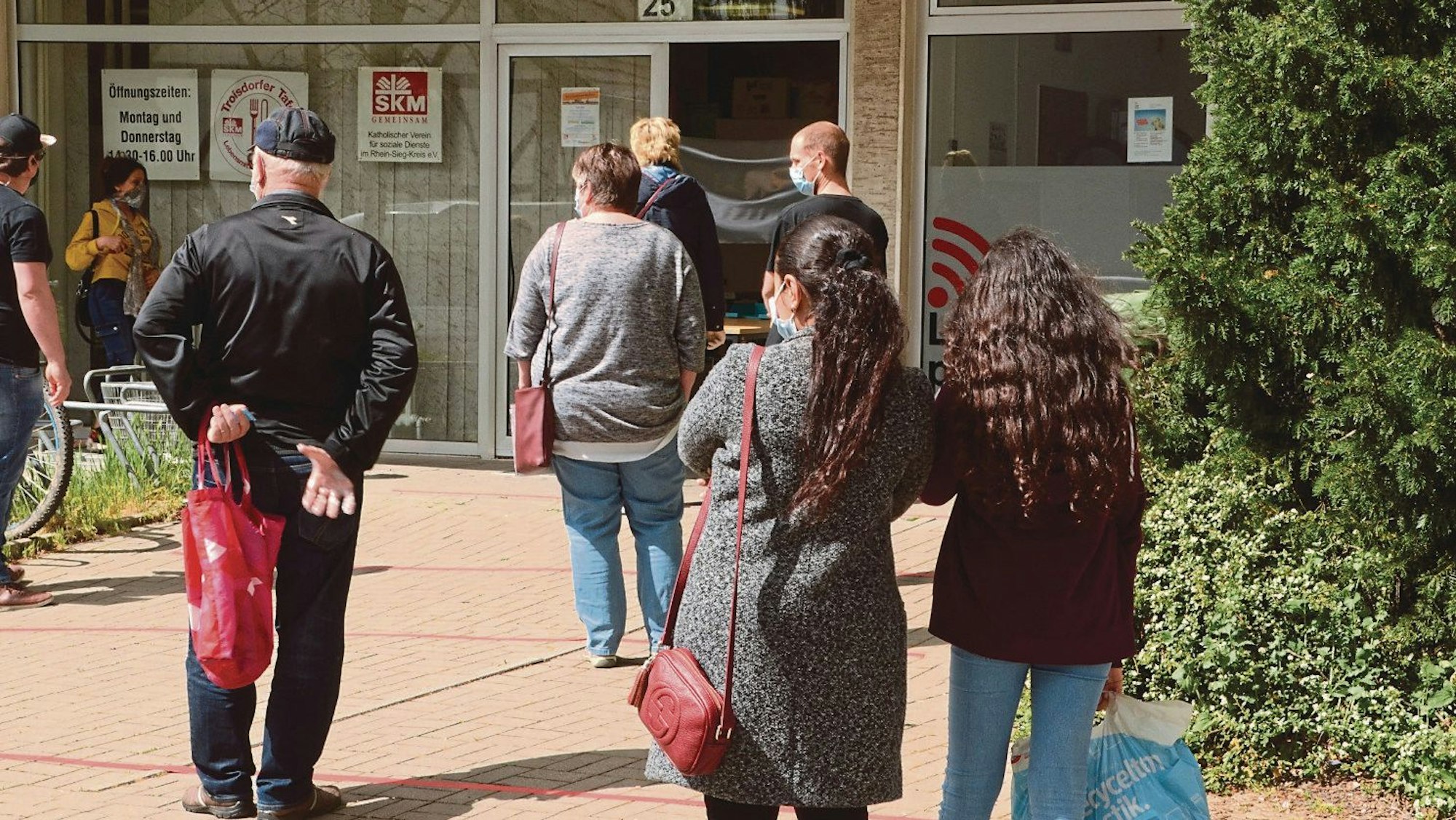 Vor einer Ausgabestelle für Lebensmittel warten Menschen. Sie wenden dem Fotografen den Rücken zu.