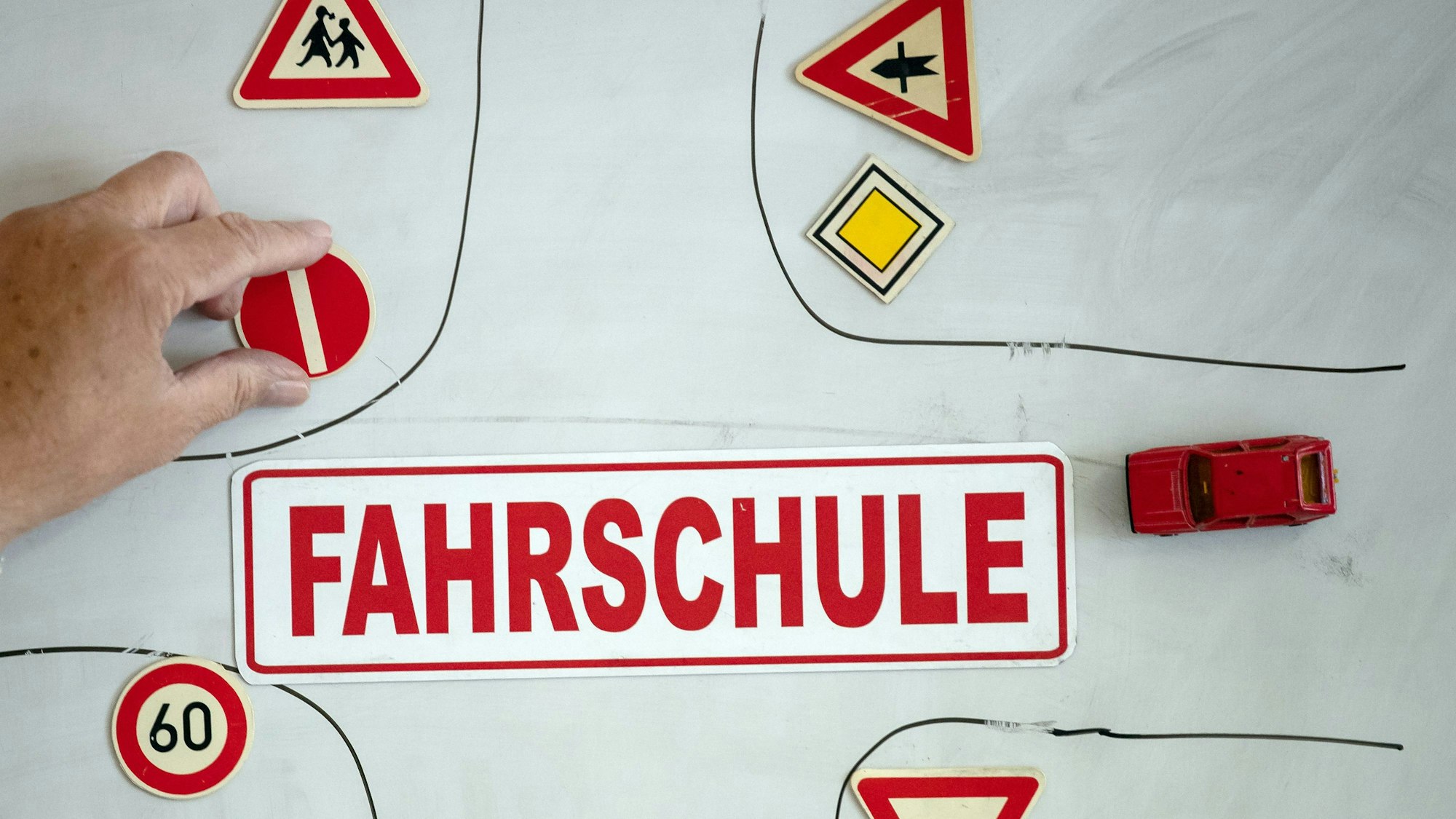 Ein Magnet mit der Aufschrift „Fahrschule“ ist an einer Wandtafel mit verschiedenen Verkehrssymbolen zu sehen.