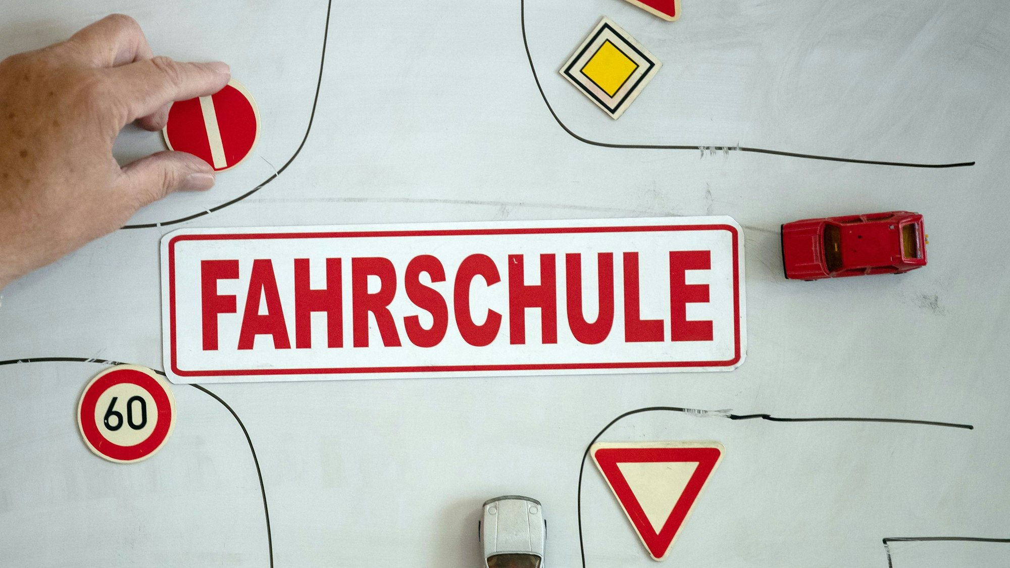 Ein Magnet mit der Aufschrift „Fahrschule“ ist an einer Wandtafel mit verschiedenen Verkehrsymbolen zu sehen.