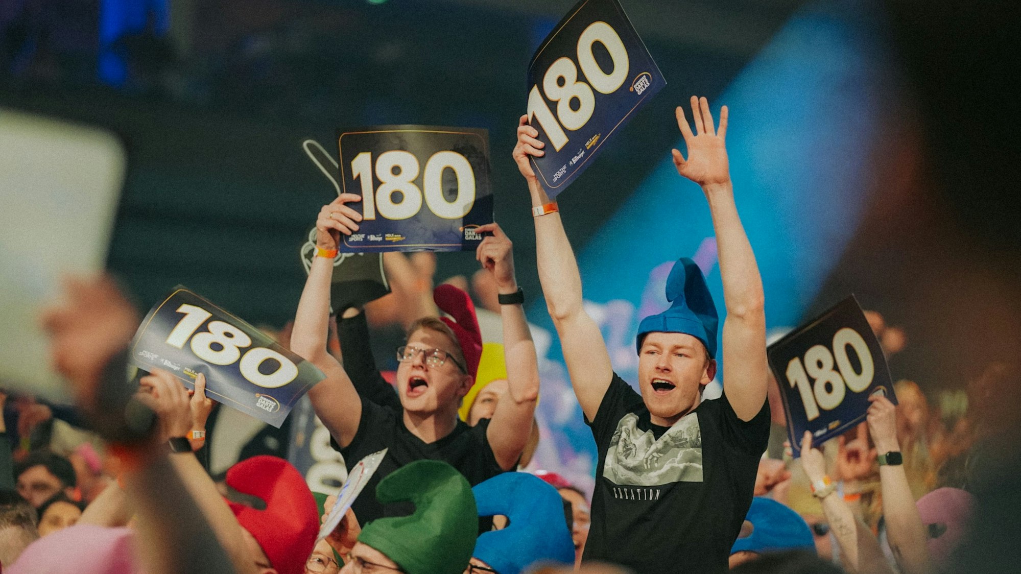 Als Zwerge verkleidete Fans halten bei der Darts-Gala in Gummersbach Schilder mit der Zahl 180 in die Höhe.