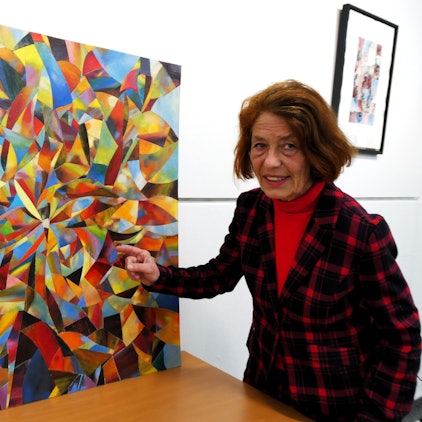 Eine Frau steht neben einem Bild, auf dem die Farben geradezu explodieren.