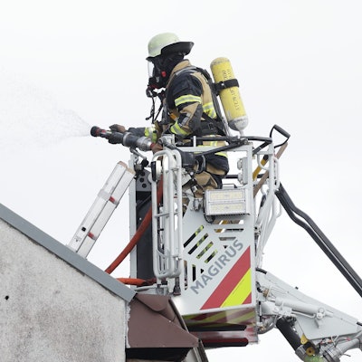 Solingen: Ein Feuerwehrmann steht an einem Mehrfamilienhaus, in dem es gebrannt hat, im Korb einer Drehleiter und bekämpft Brandnester.