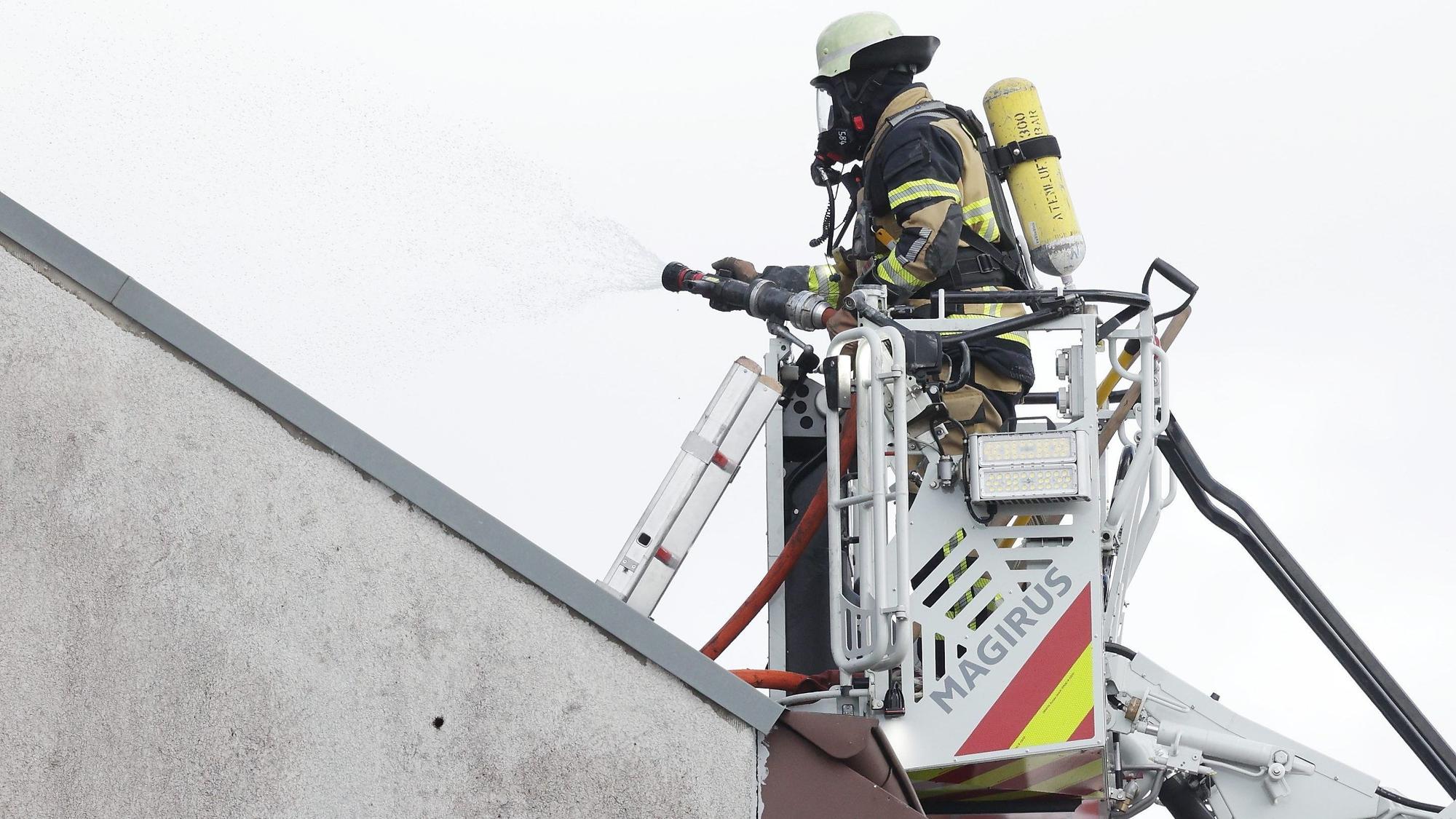 Solingen: Ein Feuerwehrmann steht an einem Mehrfamilienhaus, in dem es gebrannt hat, im Korb einer Drehleiter und bekämpft Brandnester.