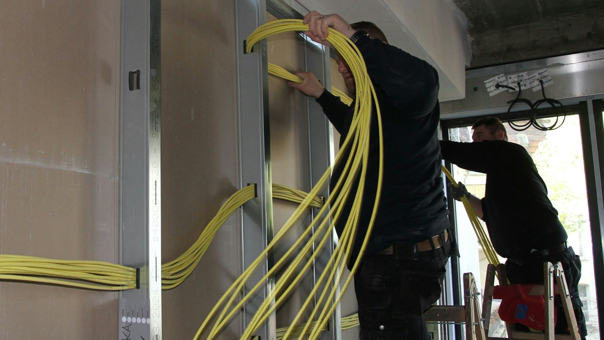 Zwei Monteure verlegen an einer Trockenbauwand gelbe Leitungskabel