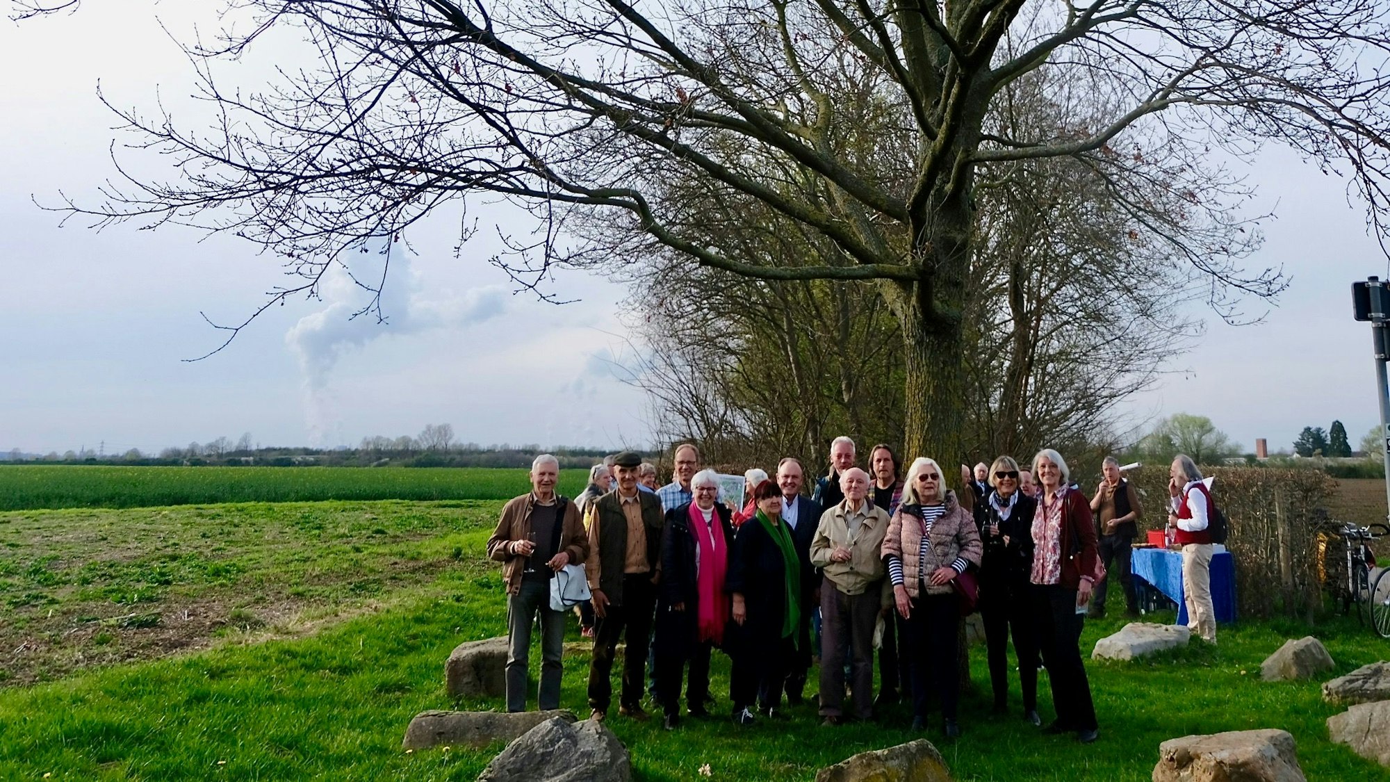 Auf einem grünen Feld stehen Politiker, Bürgervereinsmitglieder, Verwaltungsmitarbeiter und andere engagierte Bürger vor der Gründungseiche des Landschaftsparks Belvedere.