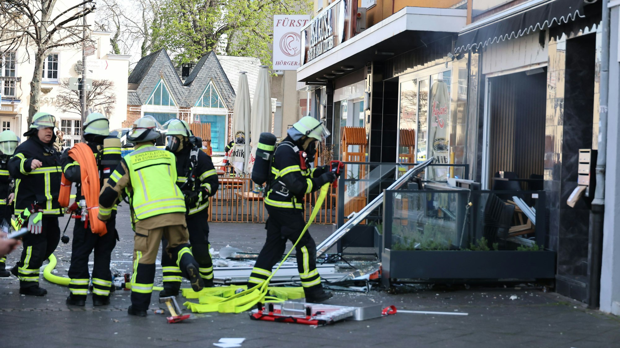 Feuerwehrleute bereiten sich auf den Innenangriff vor. Auf dem Bordstein liegen die Trümmer der Schaufensterscheibe.