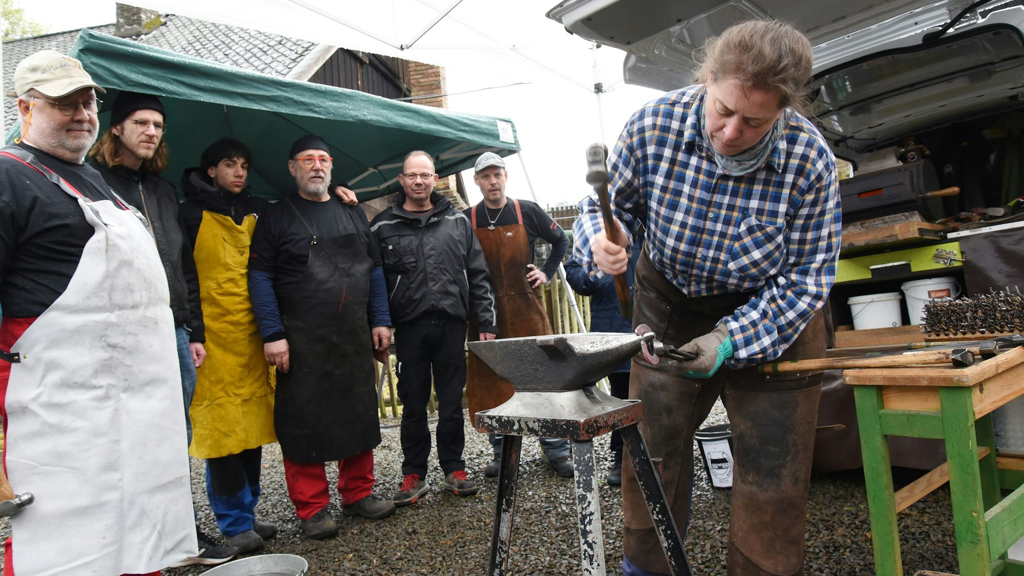 Ein Schmied in einem Museum bei der Arbeit. Besucher schauen ihm zu.