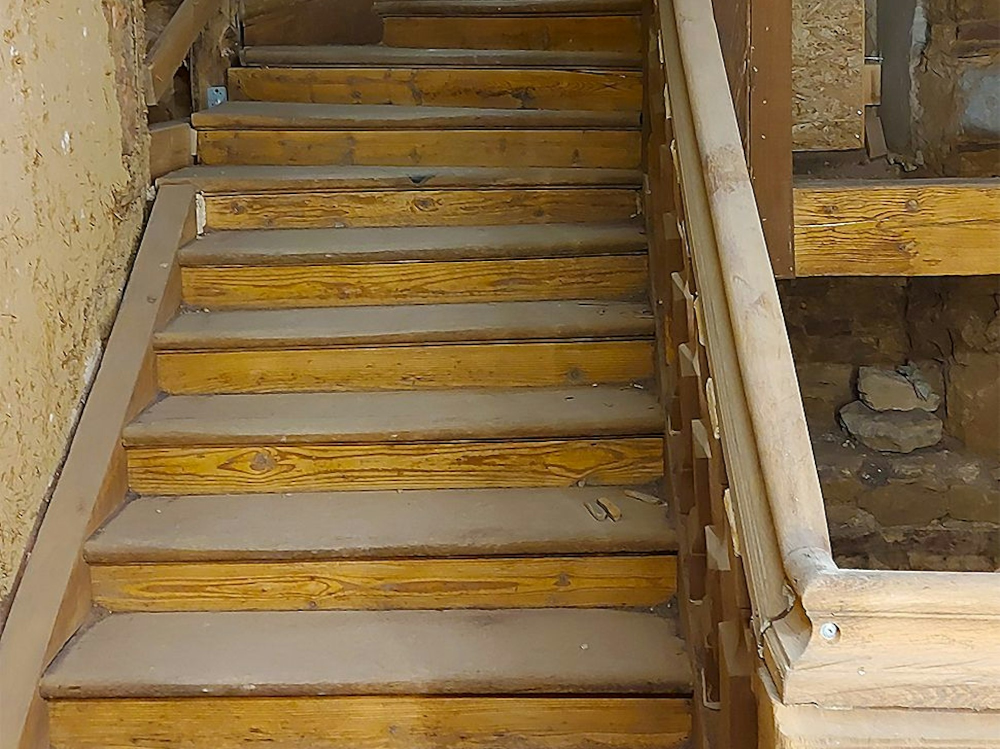 Das Bild zeigt eine alte Holztreppe, die von Staub bedeckt ist.