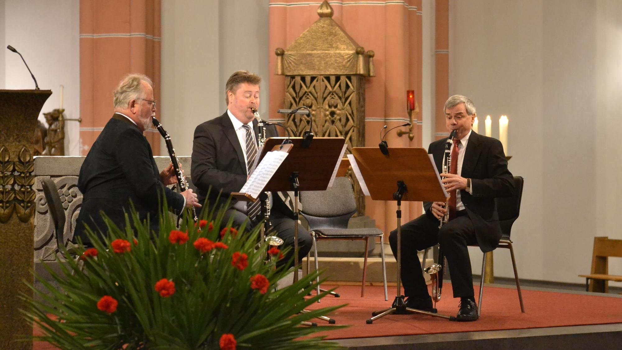 Drei Instrumentalisten musizieren vor dem Altar in der Euskirchener Herz-Jesu-Kirche. Im Vordergrund Blumen, im Hintergrund Kerzen.