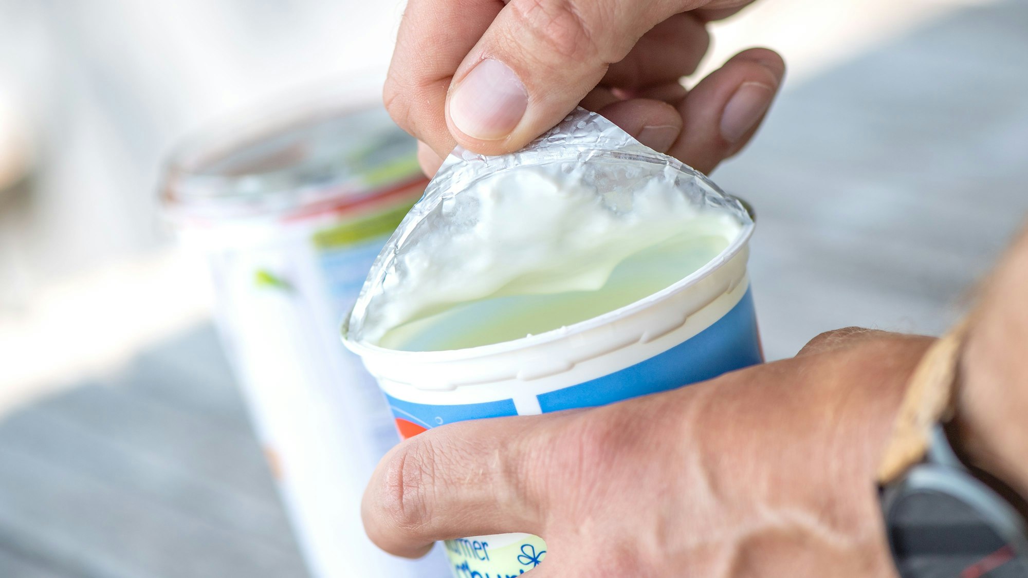Eine Person löst den Aluminiumdeckel von einem Plastikbecher.