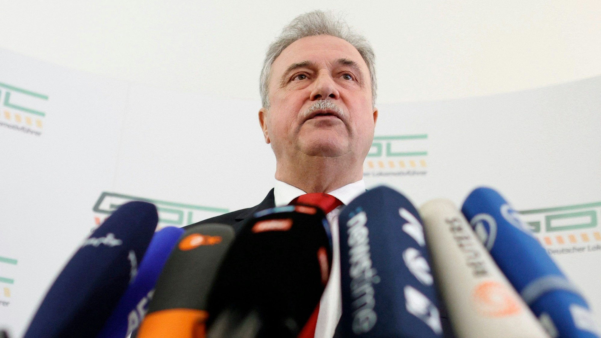 Claus Weselsky, Vorsitzender der Gewerkschaft Deutscher Lokomotivführer (GDL), präsentiert die Einigung mit der Deutschen Bahn nach monatelangen Warnstreiks. Er steht vor mehreren Fernsehmikrofonen, im Hintergrund sind Logos der GDL zu sehen.