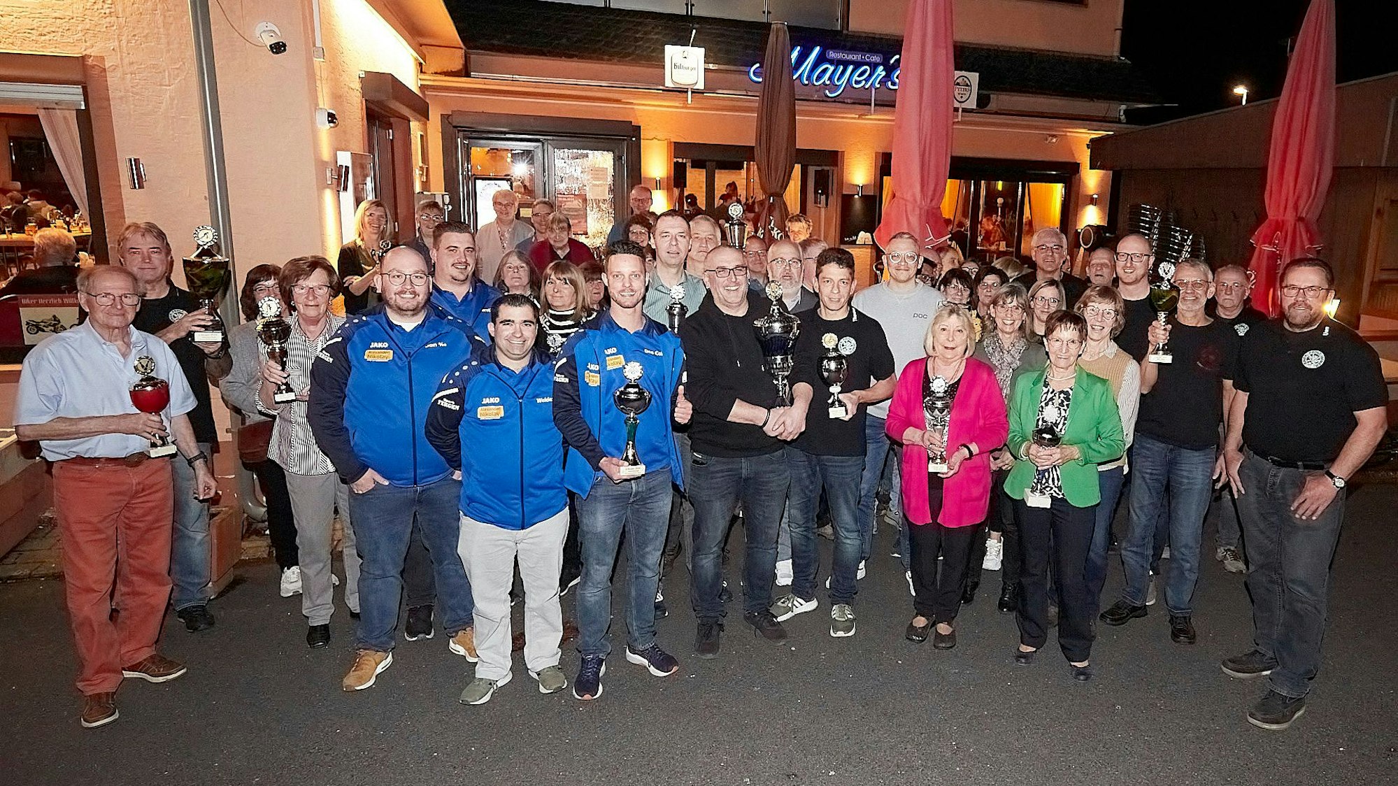 Zahlreiche Frauen und Männer stehen vor dem Restaurant Mayer's in Schleiden. Einige halten Pokale in den Händen.