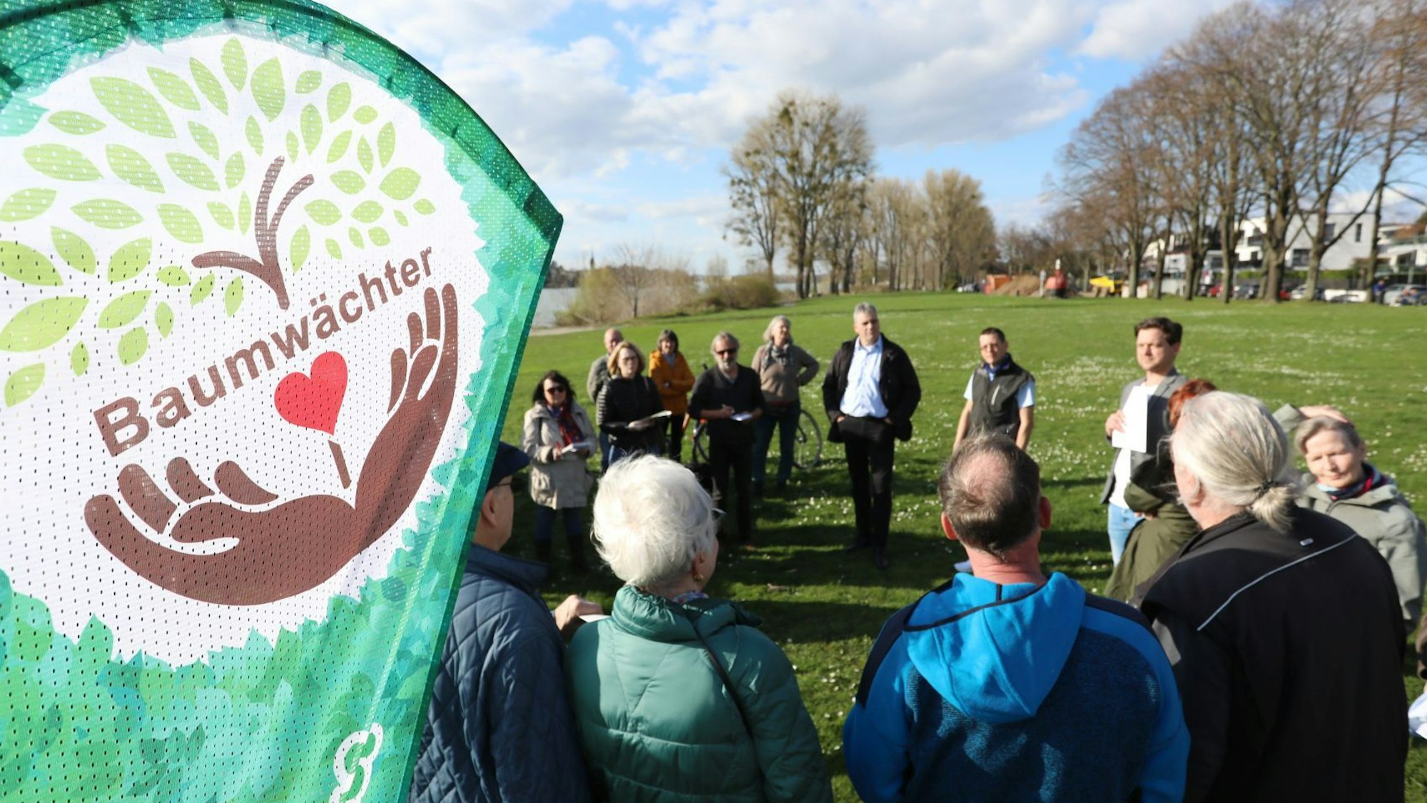 Eine Gruppe von Menschen steht im Kreis auf einer Wiese, am Rand steht ein Banner mit dem Aufdruck Baumwächter.