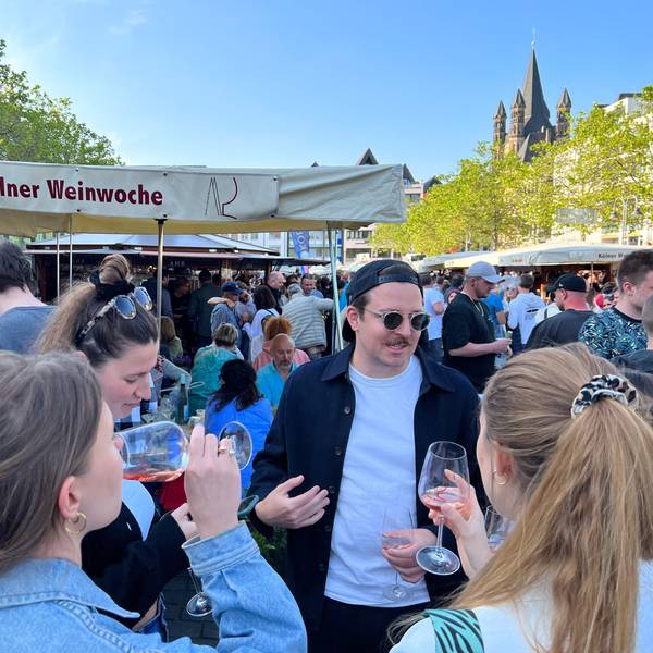 Eine Menschenmenge steht auf dem Heumarkt. Personen trinken Wein.