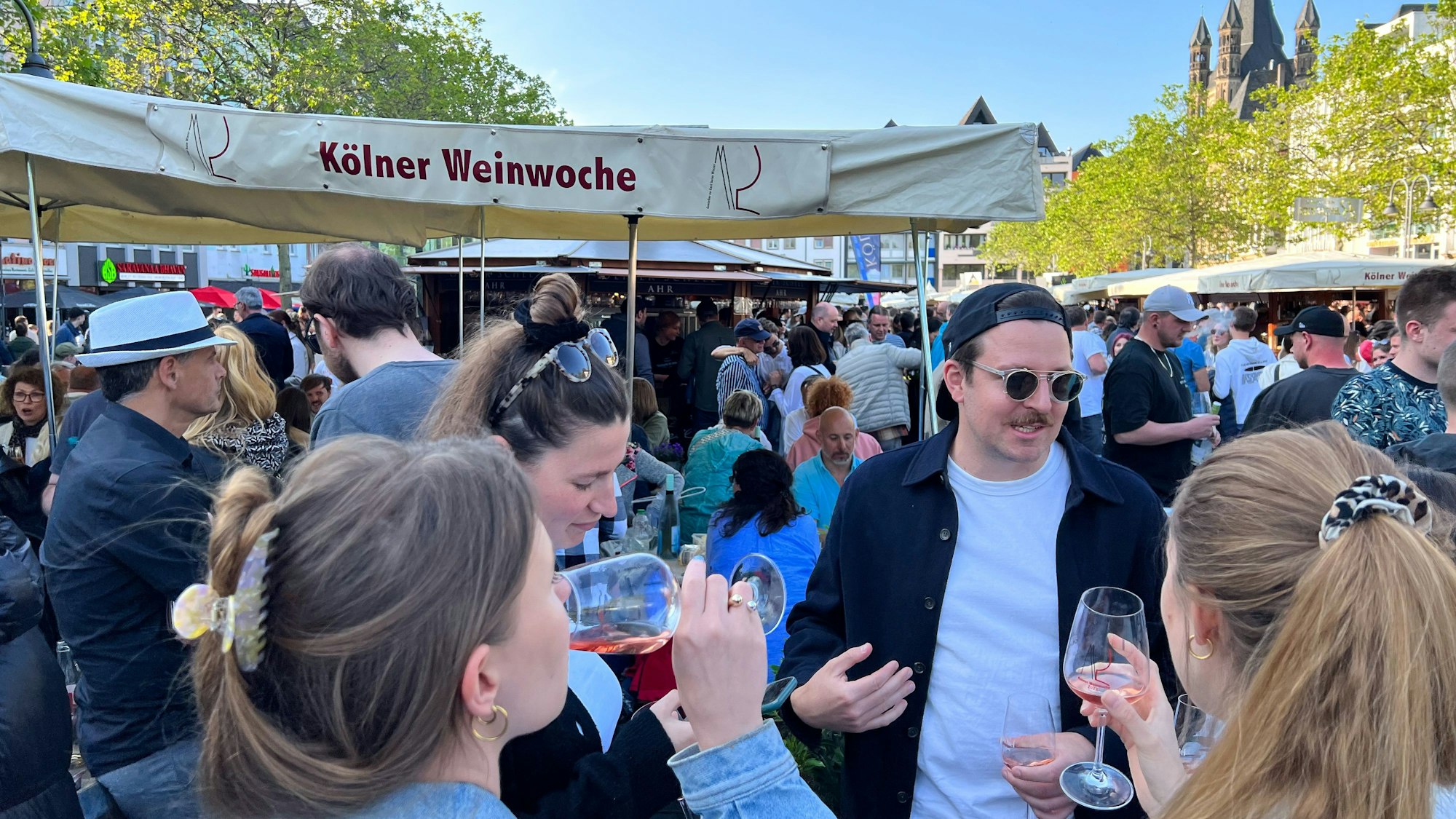 Eine Menschenmenge steht auf dem Heumarkt. Personen trinken Wein.