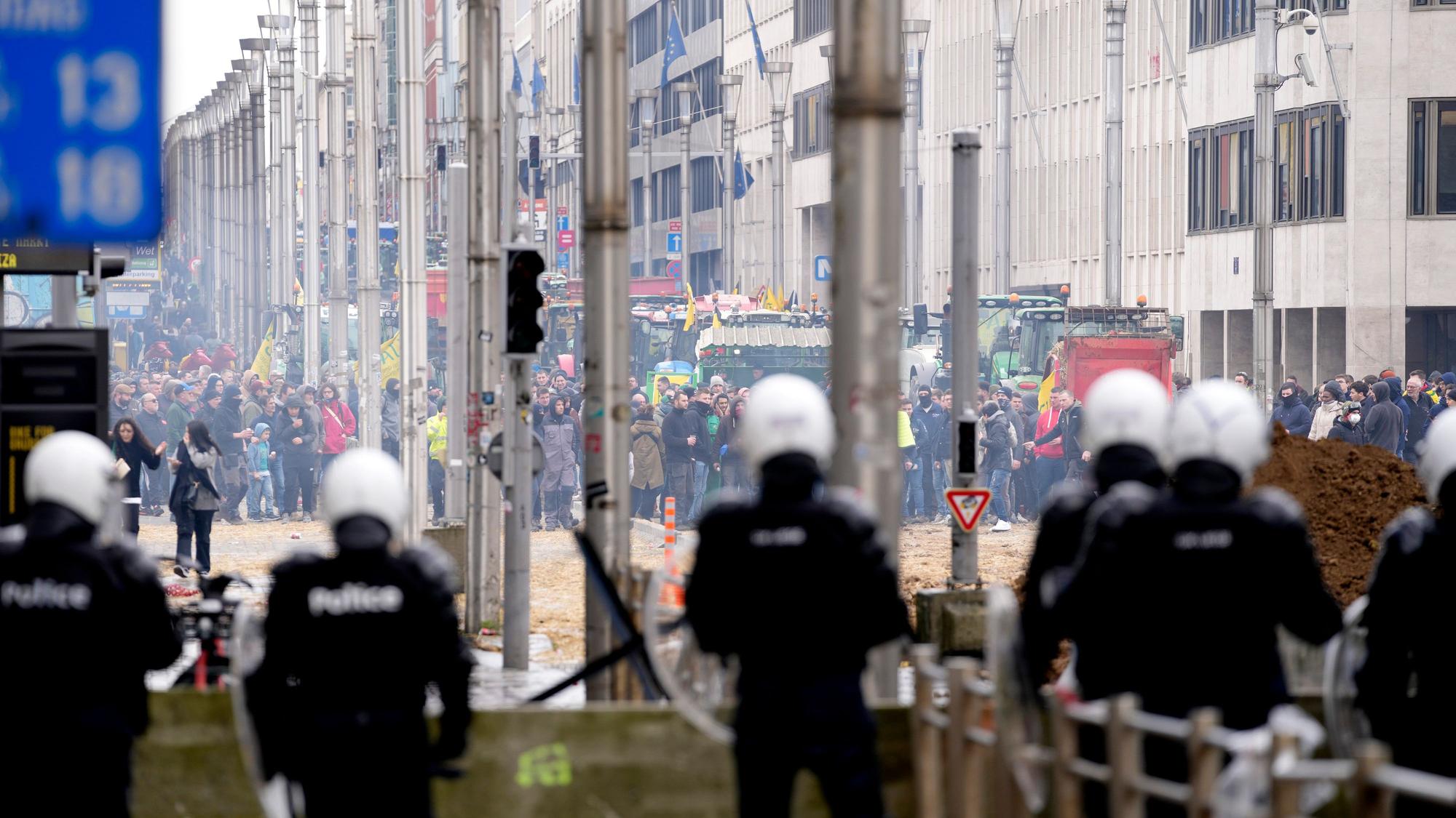 Brüssel: Polizisten patrouillieren hinter einer Absperrung, während Landwirte vor dem Gebäude des Europäischen Rates protestieren.