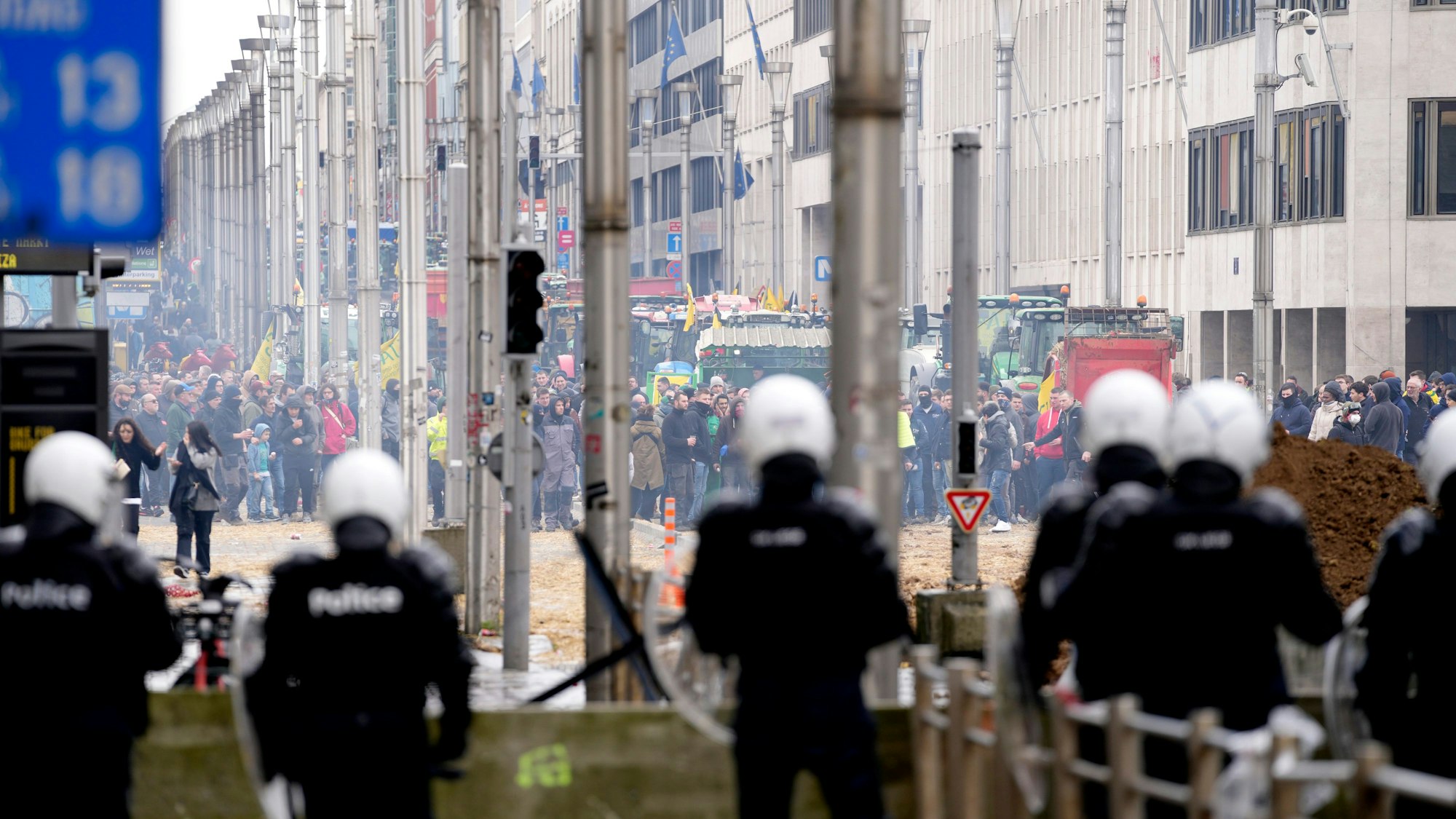Brüssel: Polizisten patrouillieren hinter einer Absperrung, während Landwirte vor dem Gebäude des Europäischen Rates protestieren.