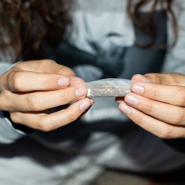 Eine junge Frau rollt nachts einen Marihuana-Joint in einer Straße. Zu sehen sind ihre Hände, in denen sie eine Cannabis-Zigarette hält.