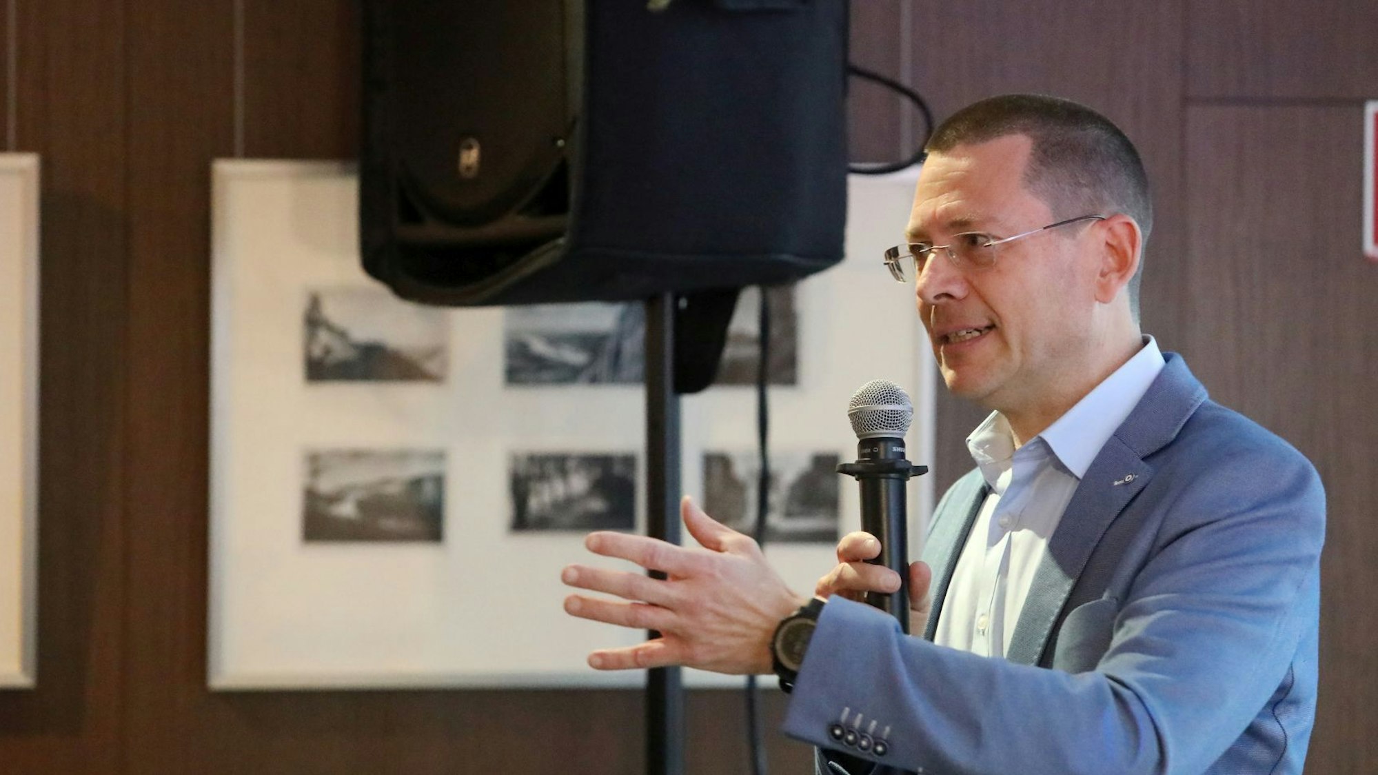 Ein Mann mit Mikrofon in der Hand steht neben einem Lautsprecher.