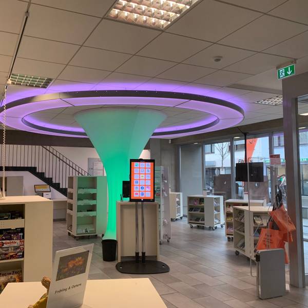 Ein Blick in das Erdgeschoss der Bibliothek. Die Lichtskulptur im Zentrum ist von Regalschränken mit Büchern und anderen Medien umgeben.