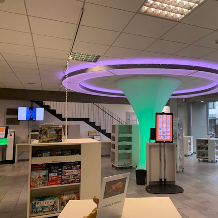 Ein Blick in das Erdgeschoss der Bibliothek. Die Lichtskulptur im Zentrum ist von Regalschränken mit Büchern und anderen Medien umgeben.