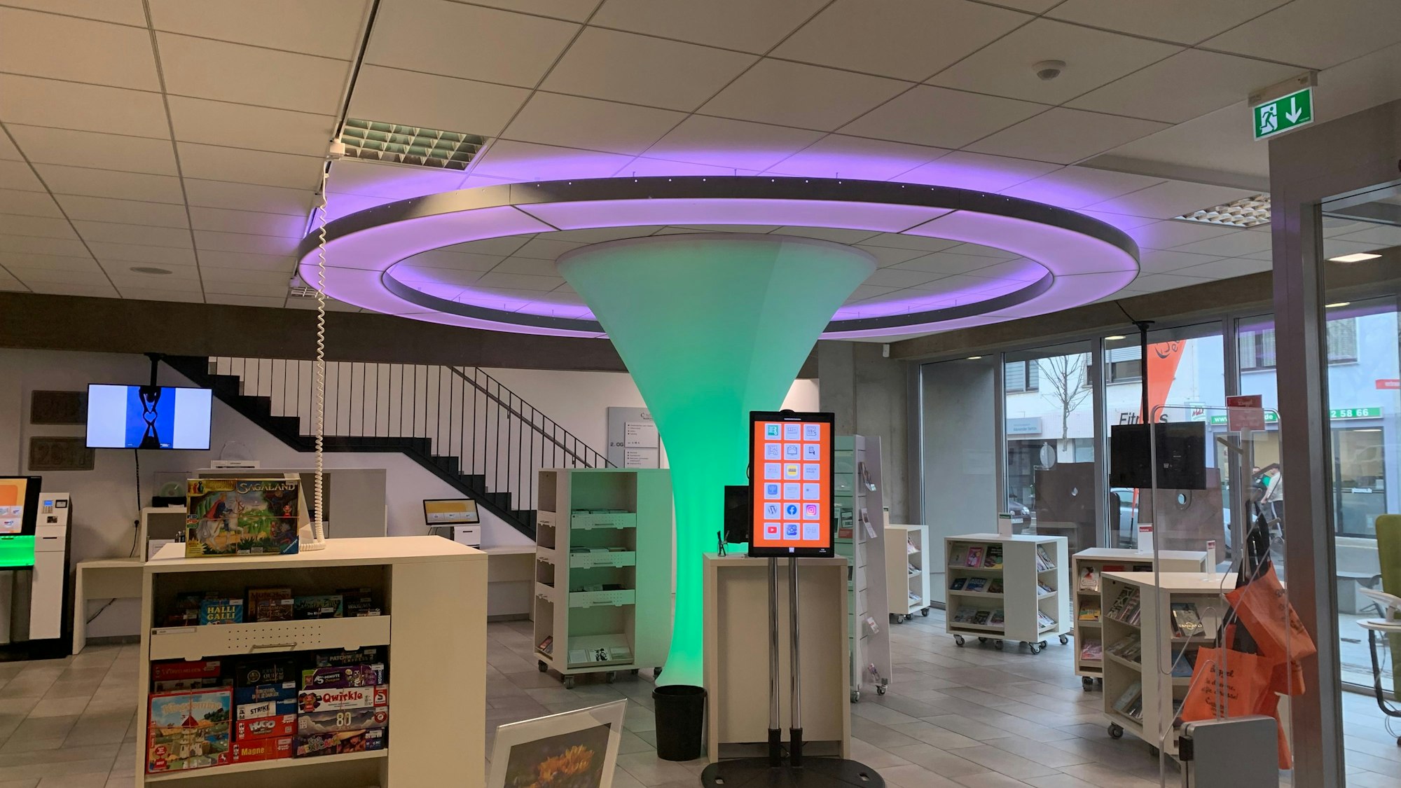 Ein Blick in das Erdgeschoss der Bibliothek. Die Lichtskulptur im Zentrum ist von Regalschränken mit Büchern und anderen Medien umgeben.
