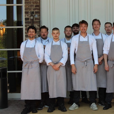 Zu sehen sind der Küchenchef und sein Team vor dem Eingang ins Restaurant.