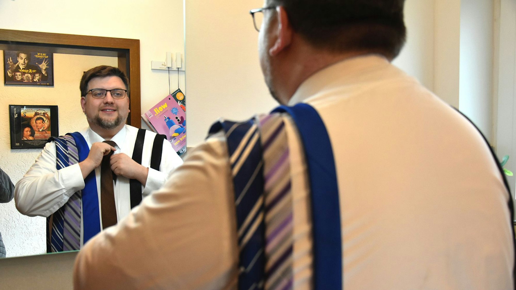 Martin Ahmann steht vor einem Spiegel und bindet eine Krawatte.