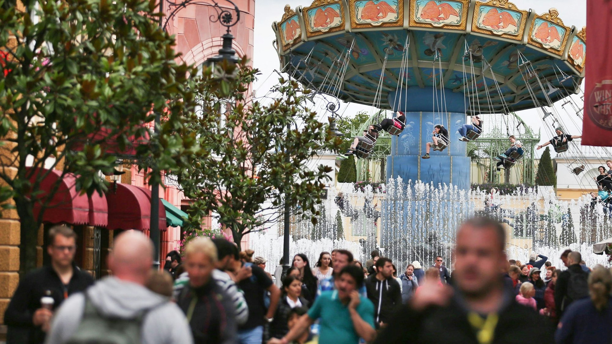 Auf dem Foto sind Besucher im Freizeitpark Phantasialand zu sehen. Im Hintergrund dreht sich ein Kettenkarussell.