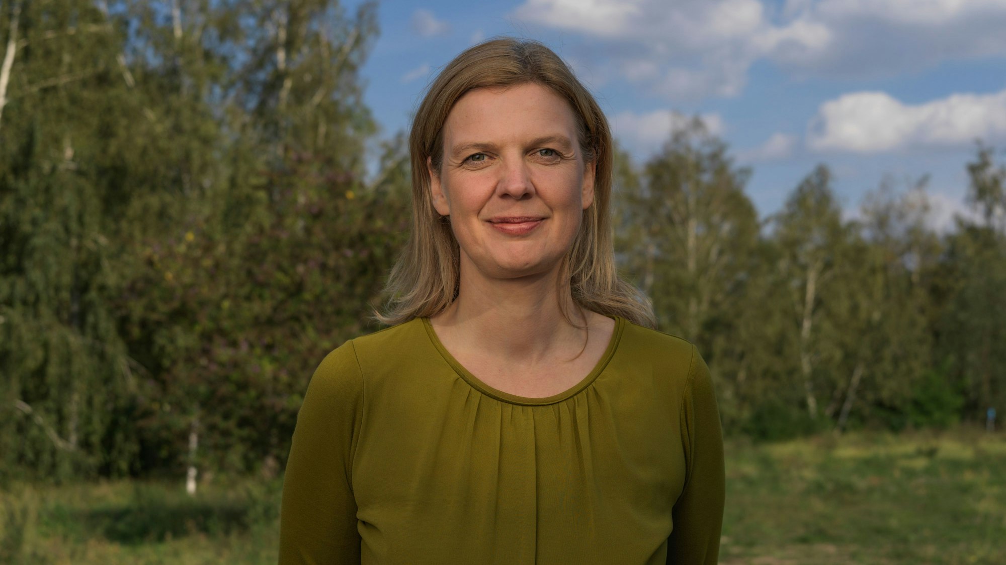 Antje Monshausen steht vor einem Hintergrund aus grünen Bäumen.