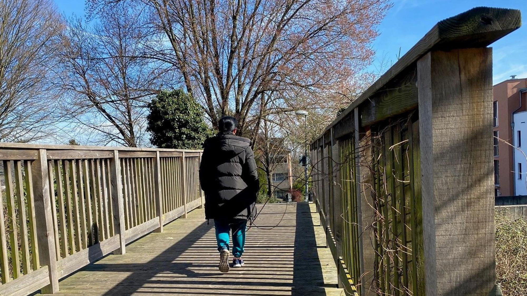 Das Bild zeigt eine Holzbrücke, über die eine Person spaziert.