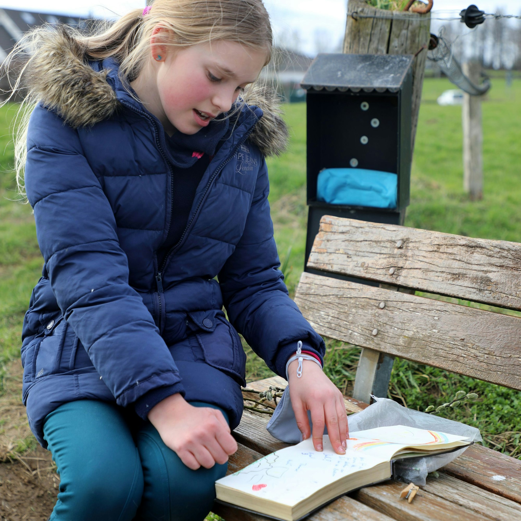 Ein Mädchen sitzt auf einer Bank und blättert in einem Buch.