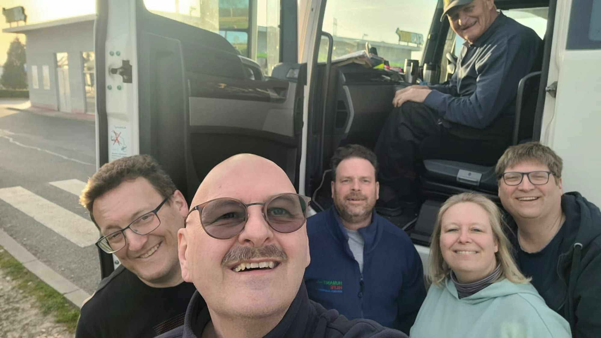 Menschen schauen an der geöffneten Fahrertür eines Lkw in eine Kamera für ein Selfie.