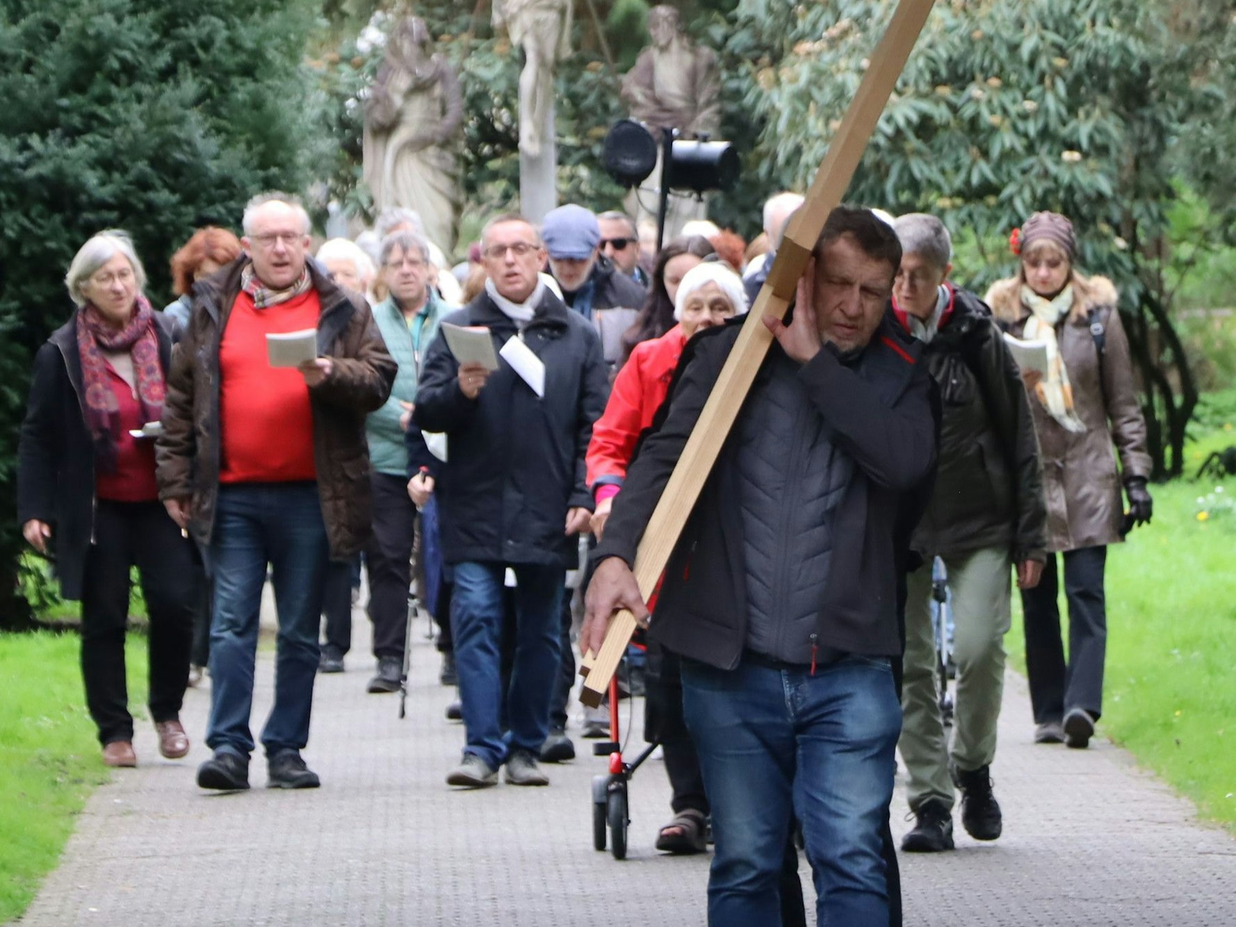 Das Bild zeigt eine Gruppe vom Menschen, die hinter einem Kreuz hergehen.