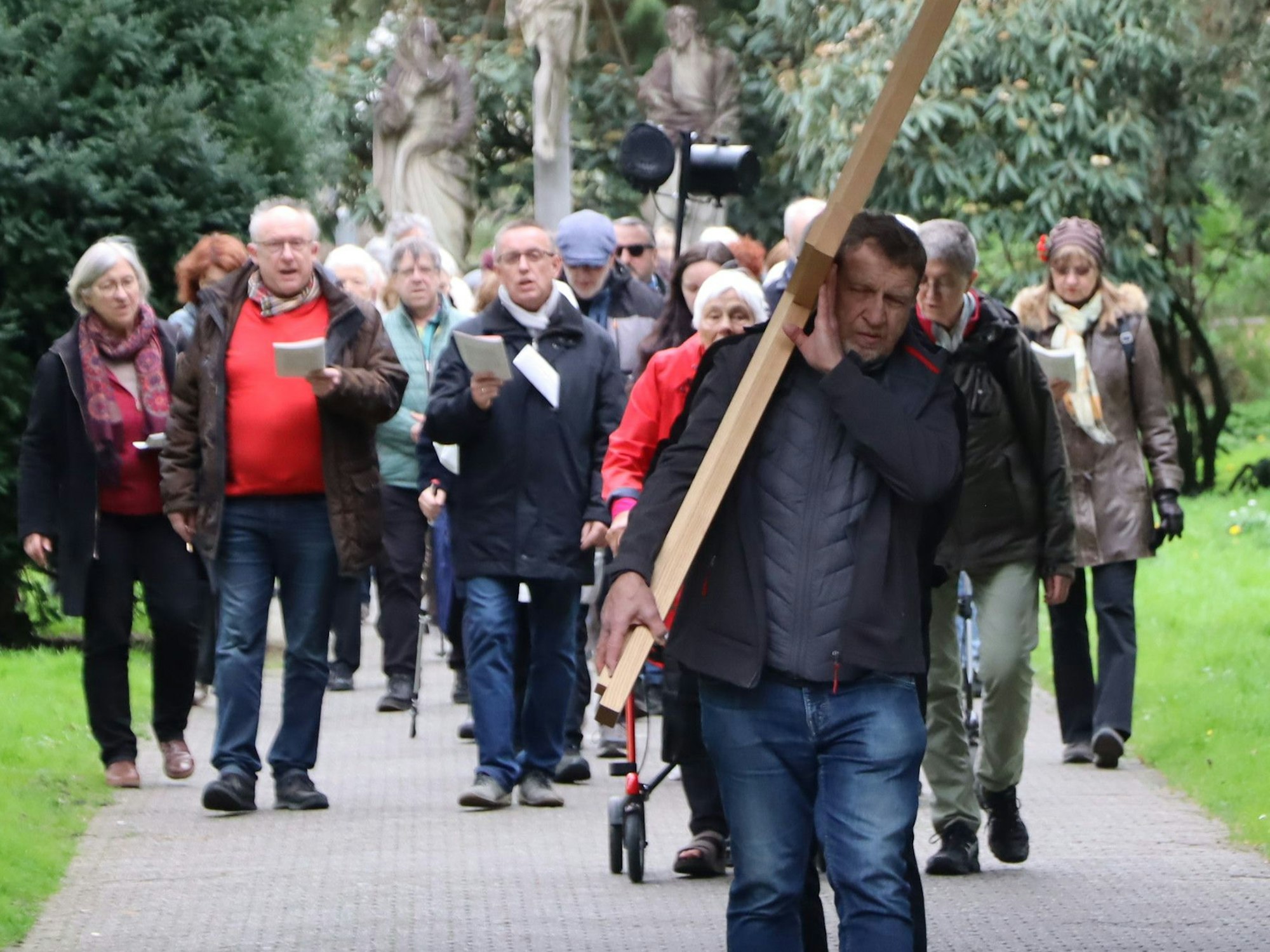 Das Bild zeigt eine Gruppe vom Menschen, die hinter einem Kreuz hergehen.