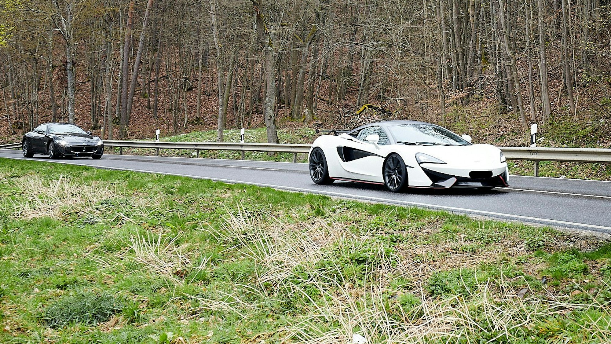 Ein weißer und ein schwarzer Sportwagen fahren hintereinander über eine Straße.