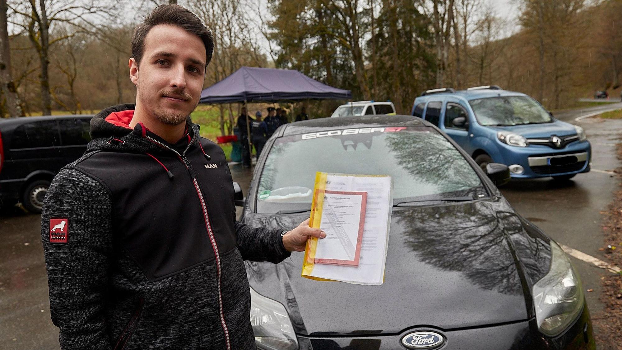 Ein junger Mann steht an seinem getunten Auto. Er hat eine Mappe mit Unterlagen in der Hand, mit denen er alle technischen Veränderungen belegen kann.