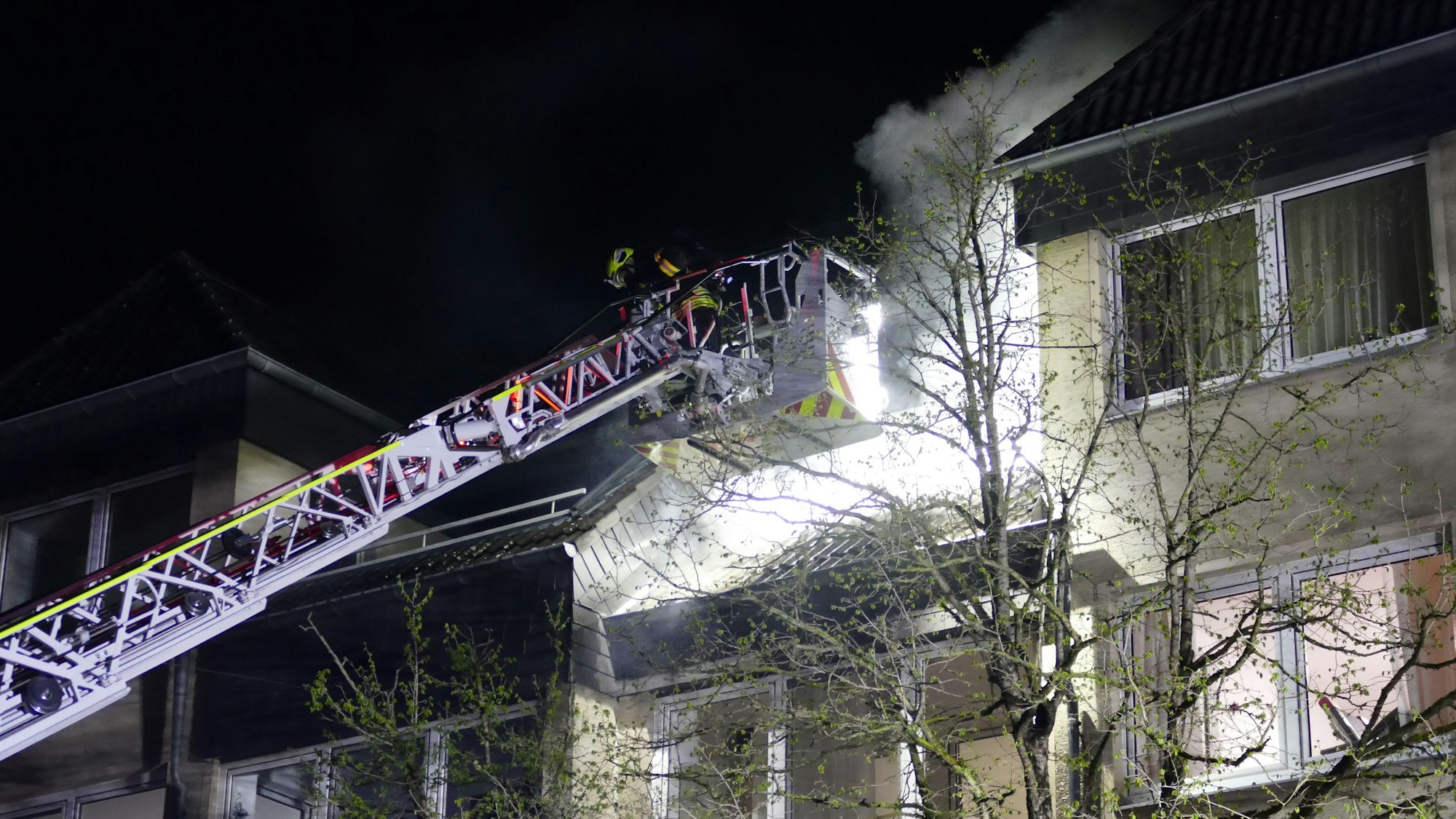 Ein Korb der Drehleiter vor einem Balkon, Qualm steigt auf.
