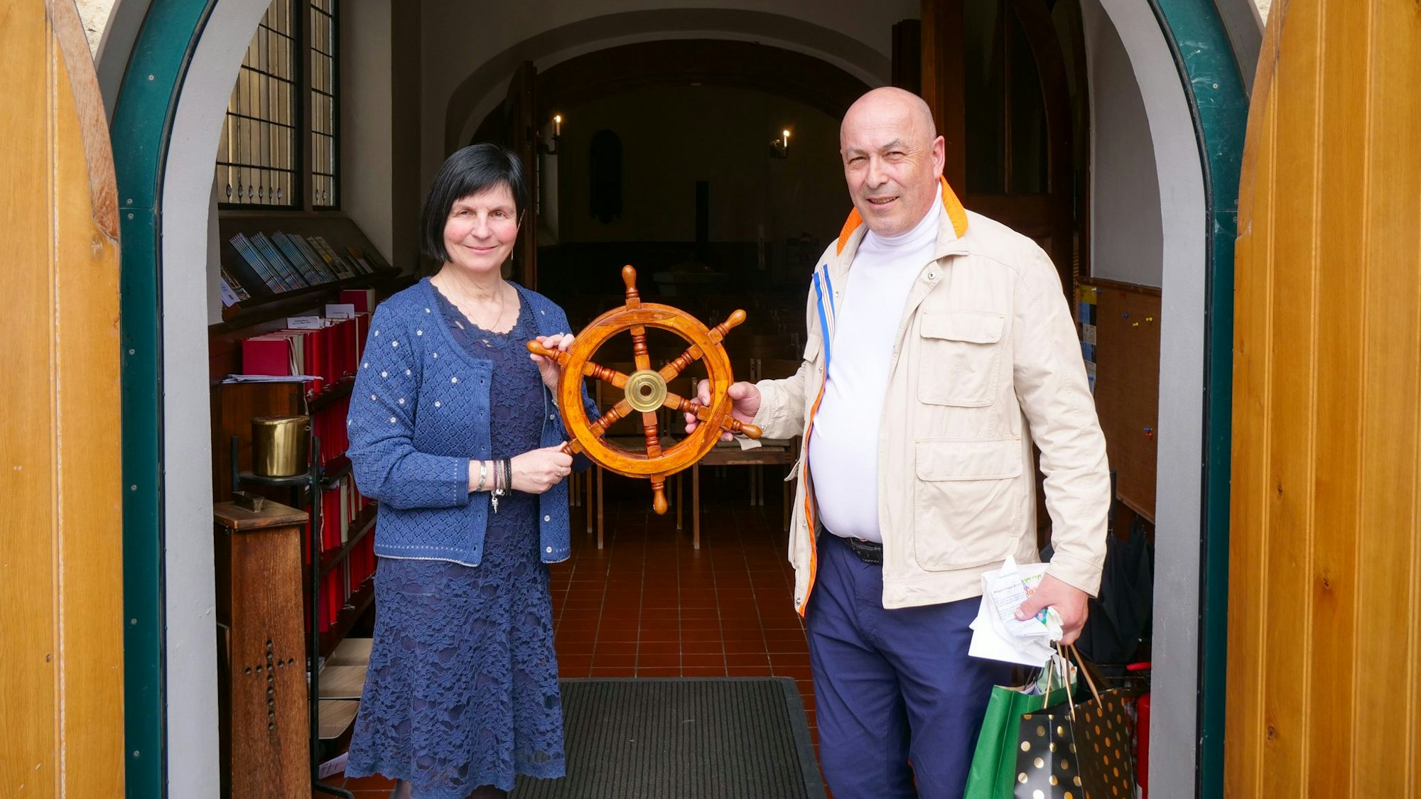 Zu sehen sind eine Frau und ein Mann, die das Steuerrad eines Schiffs halten.