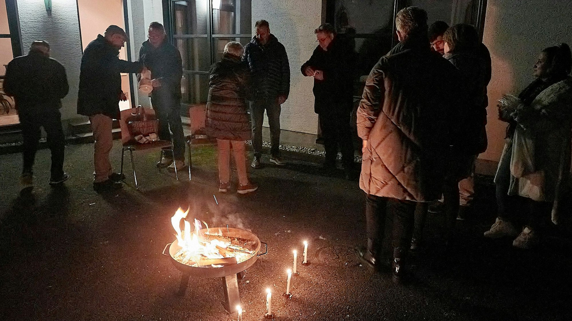 Mehrere Personen stehen in einem Hof um ein Feuer.