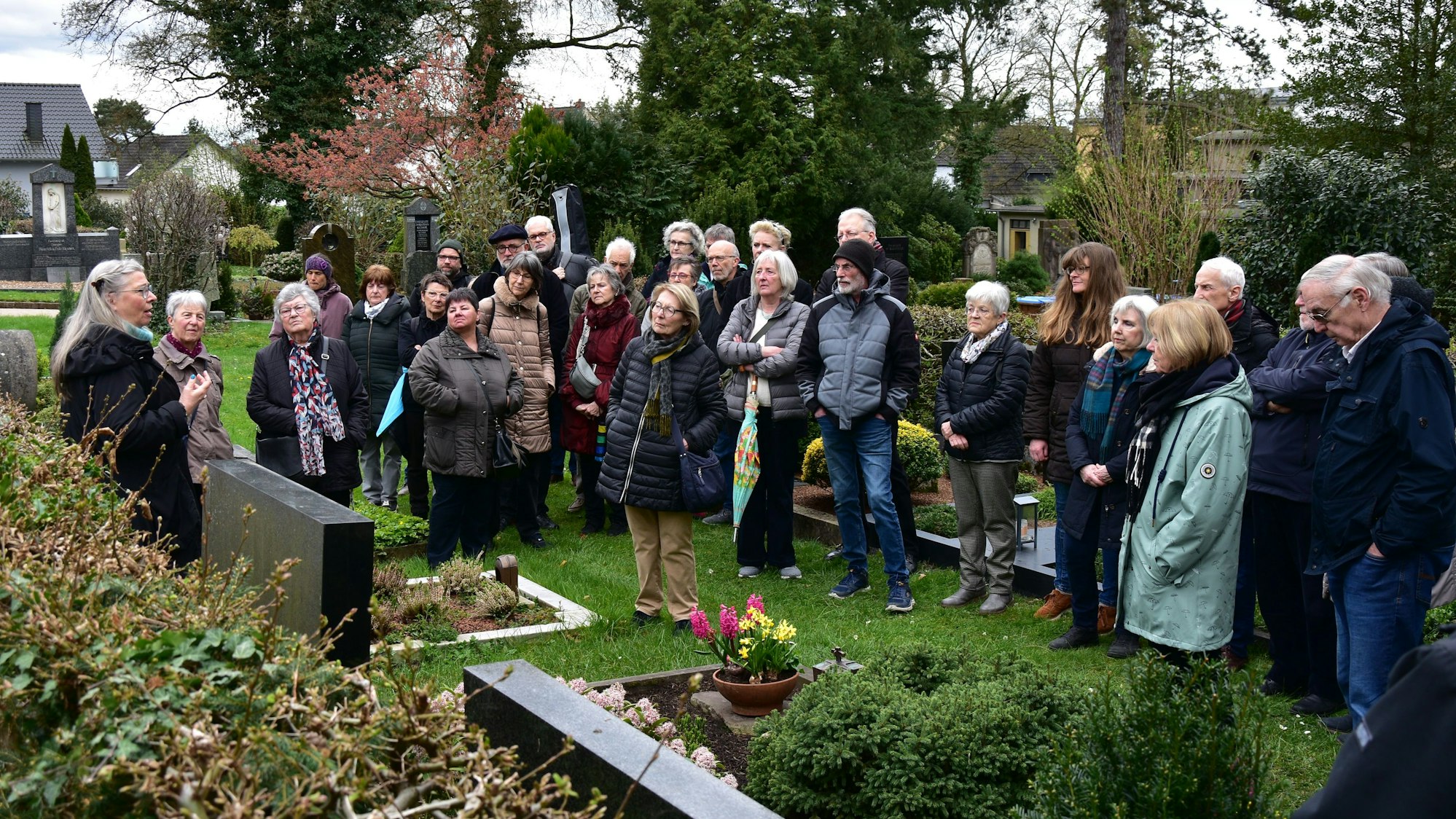 Eine Gruppe von Menschen steht vor Gräbern auf dem Friedhof.