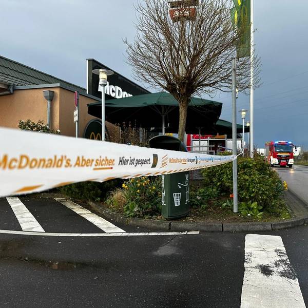 Zu sehen ist die abgesperrte Filiale eines Schnellrestaurants, im Hintergrund fährt die Feuerwehr.