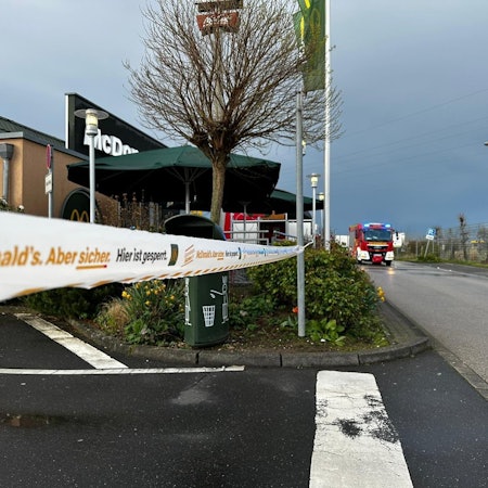 Zu sehen ist die abgesperrte Filiale eines Schnellrestaurants, im Hintergrund fährt die Feuerwehr.