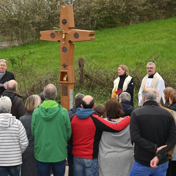 Viele Menschen stehen vor einem Wegekreuz.