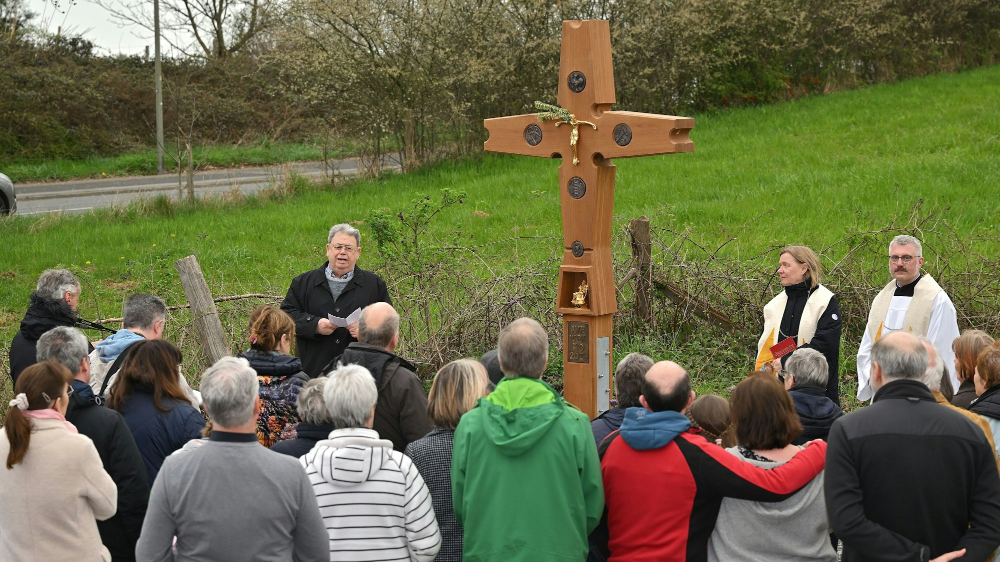 Viele Menschen stehen vor einem Wegekreuz.