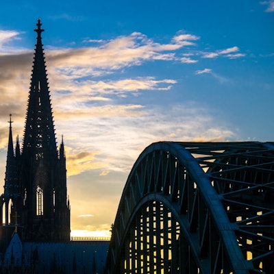 Die Sonne geht hinter dem Kölner Dom und der Hohenzollernbrücke unter, mehrere Wolken schieben sich vor den blauen Himmel. (Symbolbild)